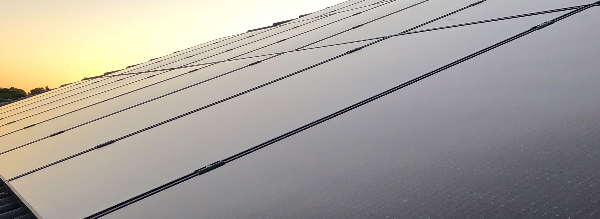 Nahaufnahme einer schwarzen Photovoltaikanlage auf einem Dach bei Sonnenuntergang, im Hintergrund ein farbenfroher Himmel